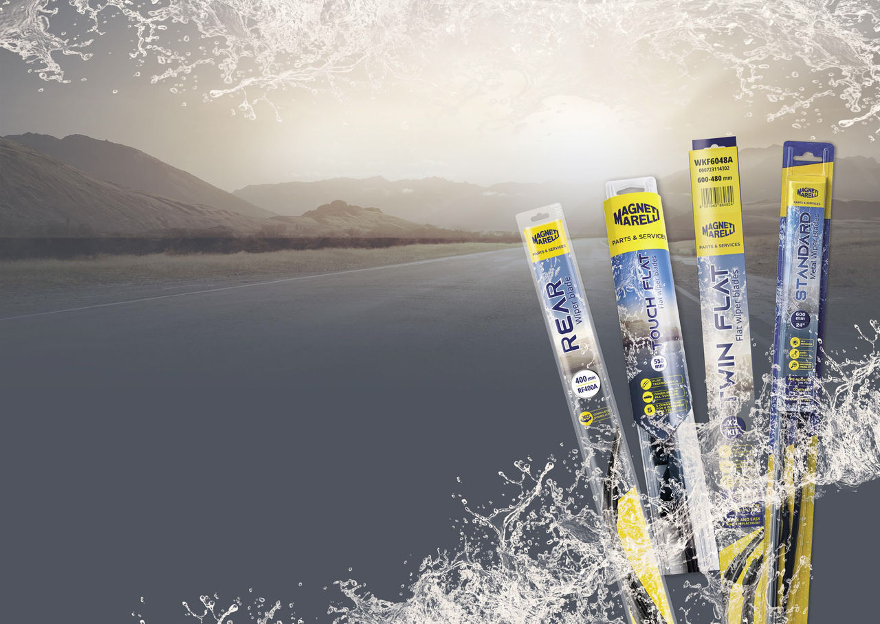 Sunrise over the road Vier modellen van Magneti Marelli ruitenwisserbladen in hun verpakking, met een bergweg op de achtergrond en regendruppels die het zicht door een schone voorruit simuleren.